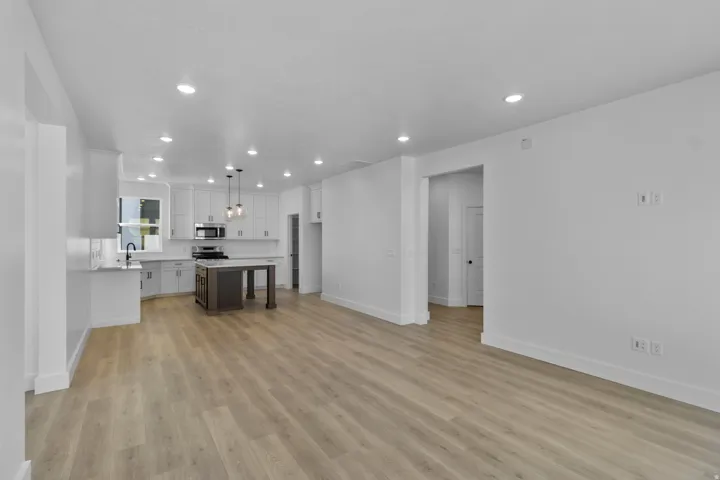 Wood-finish flooring throughout, recessed lighting, white cabinetry, dark island with light countertop, and stainless steel appliances