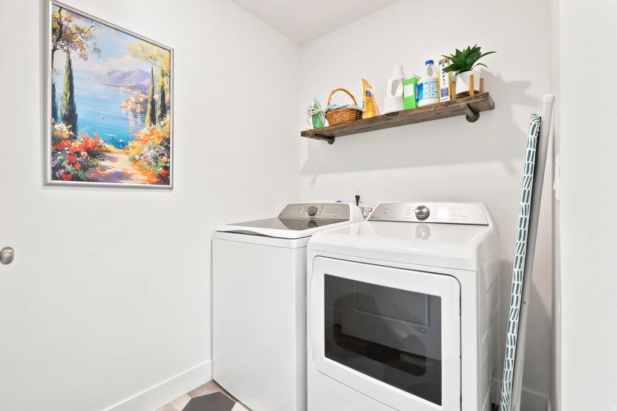 Laundry area featuring white appliances, a wood-finish floating shelf, and hexagonal floor tiling