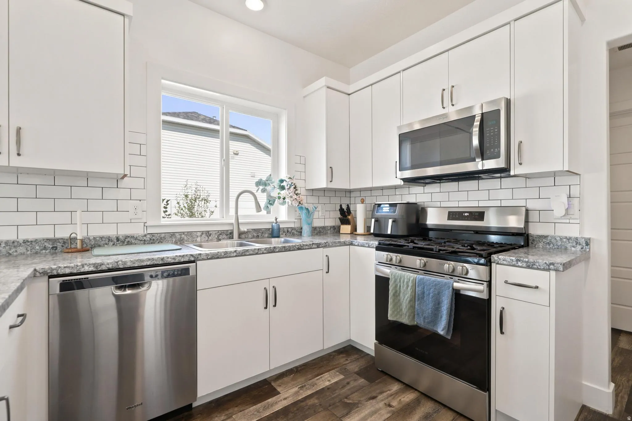 Kitchen featuring white cabinetry, stainless steel appliances, subway tile backsplash, and wood-finish flooring