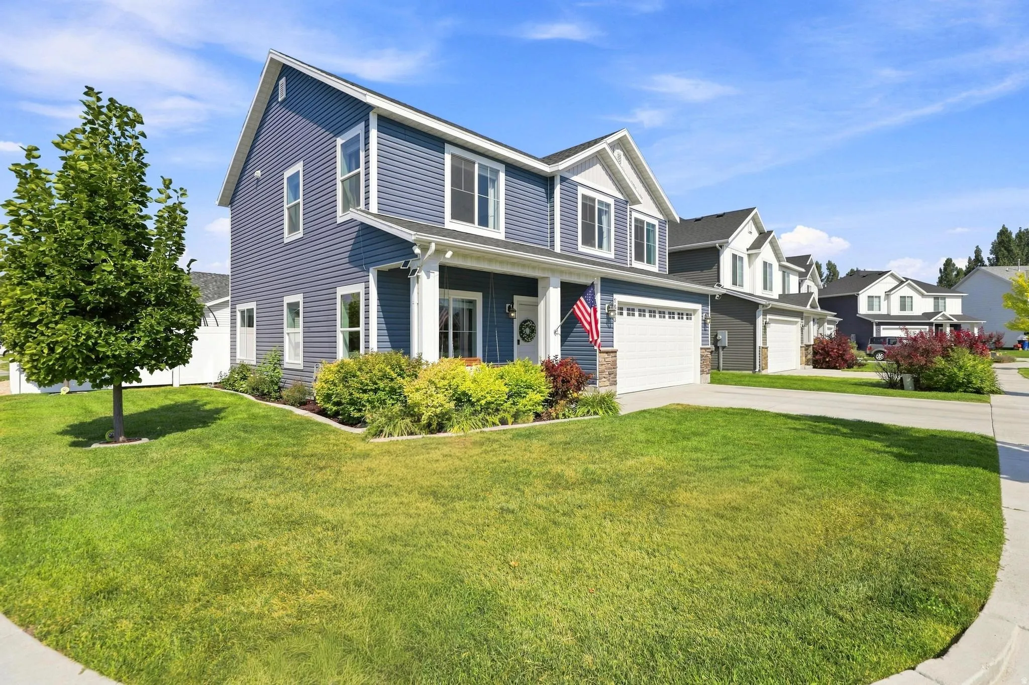 Two-story residence featuring blue siding with white trim, an attached two-car garage, established front landscaping, and a concrete driveway