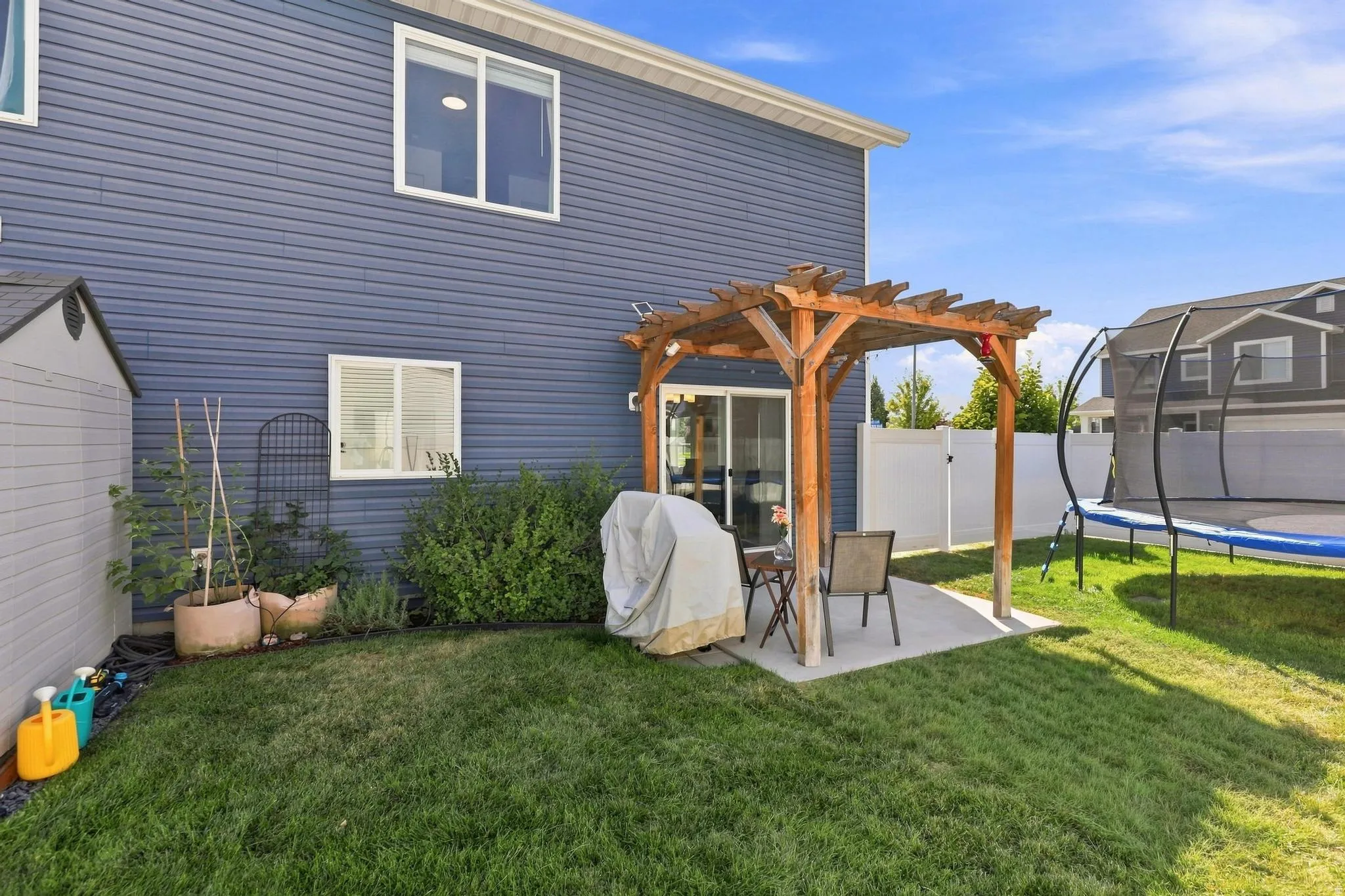 Blue horizontal siding, white trim windows, sliding glass door, wooden pergola, concrete patio