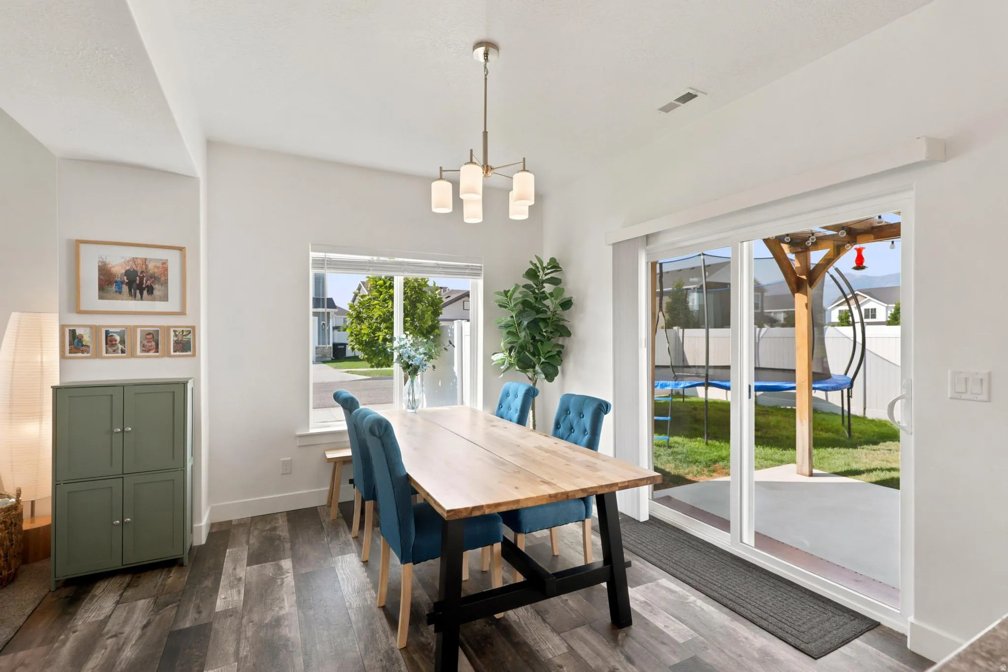 Vaulted ceiling, wood-finish flooring, contemporary chandelier, bright window, and sliding glass door to the backyard