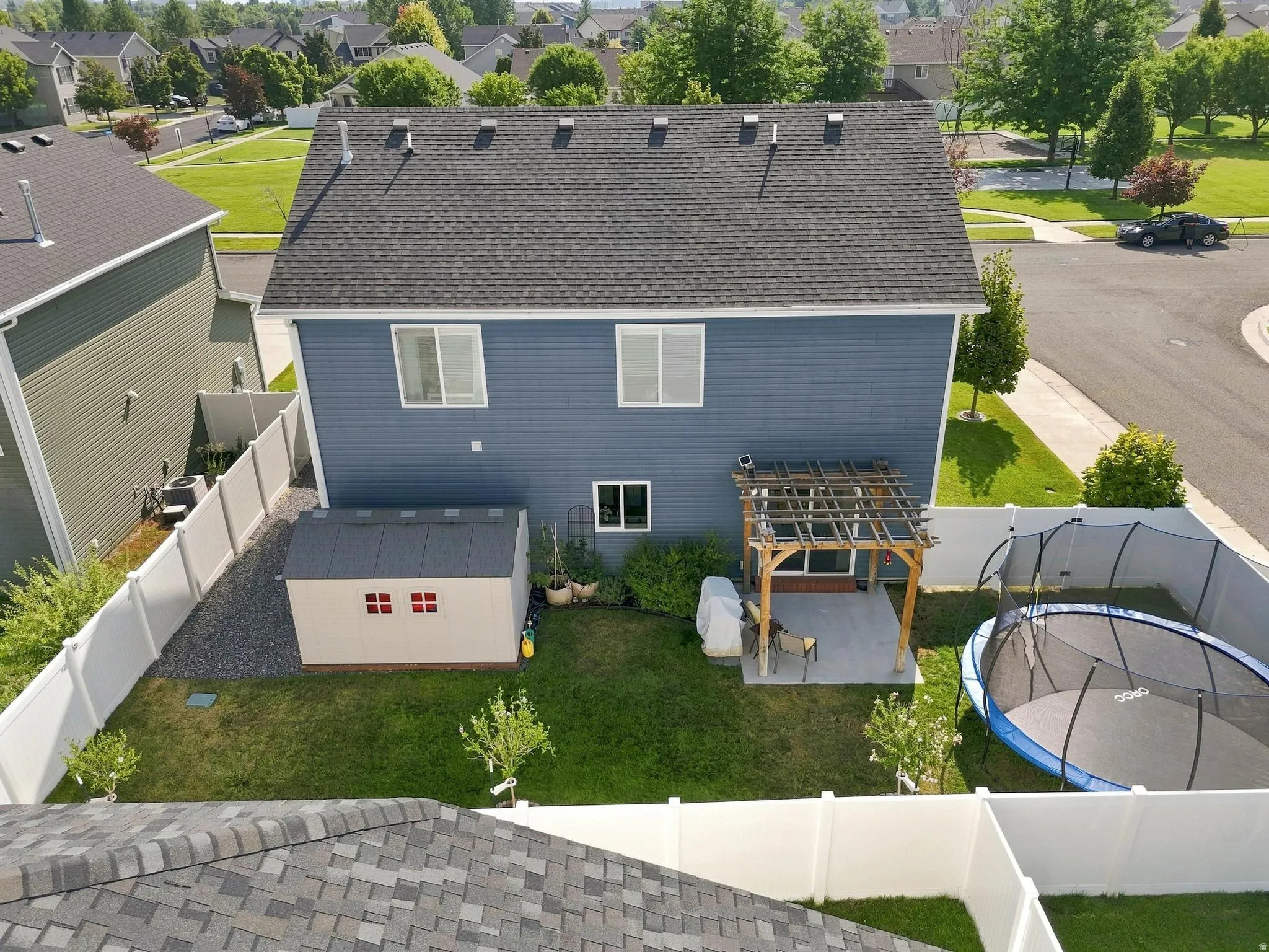 Shingled roof with multiple dormers, blue siding, a ground-level patio with a pergola, and a storage shed