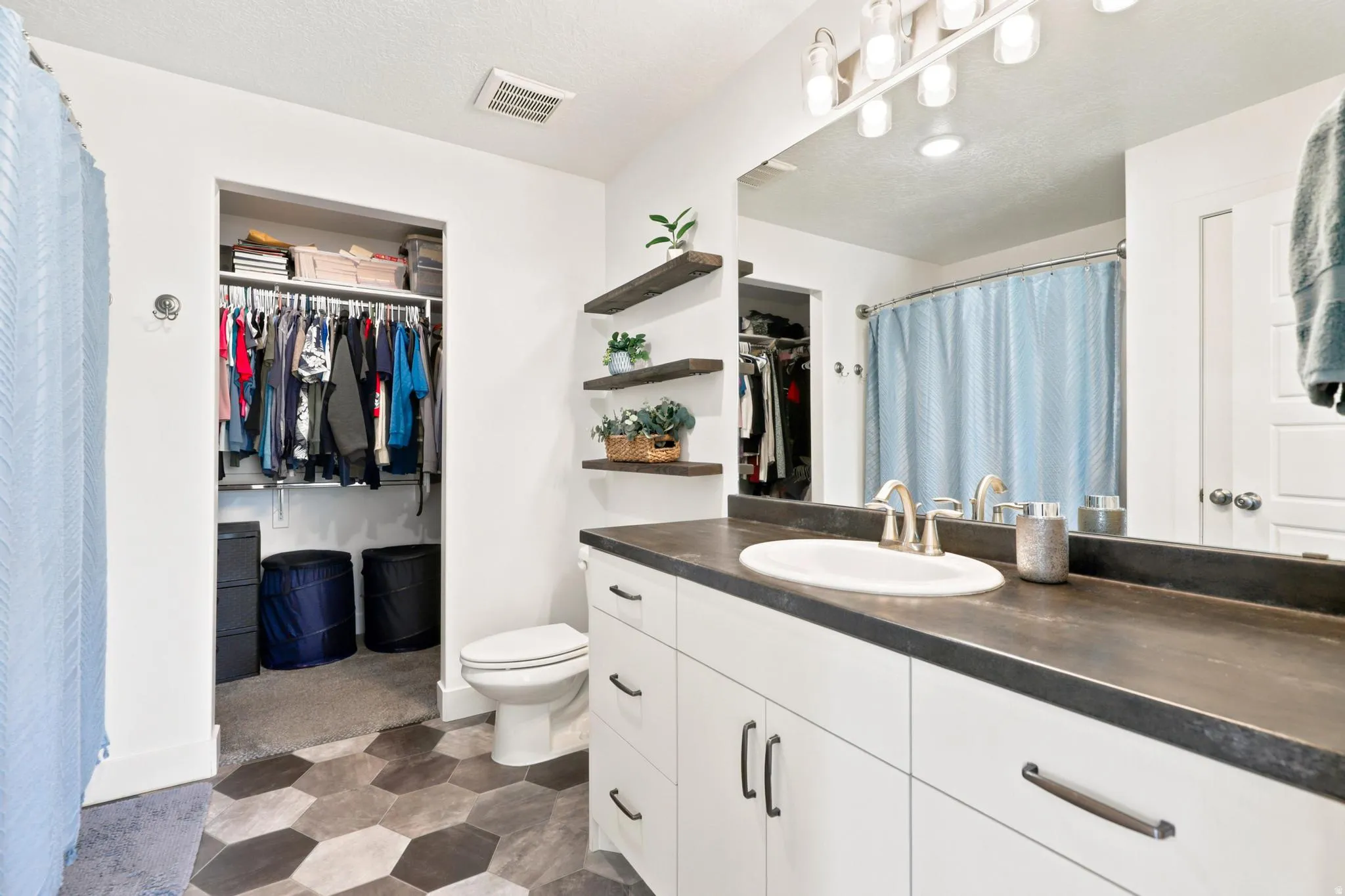 Hexagonal tile flooring, white vanity with integrated sink, dark countertop, open shelving, and walk-in closet