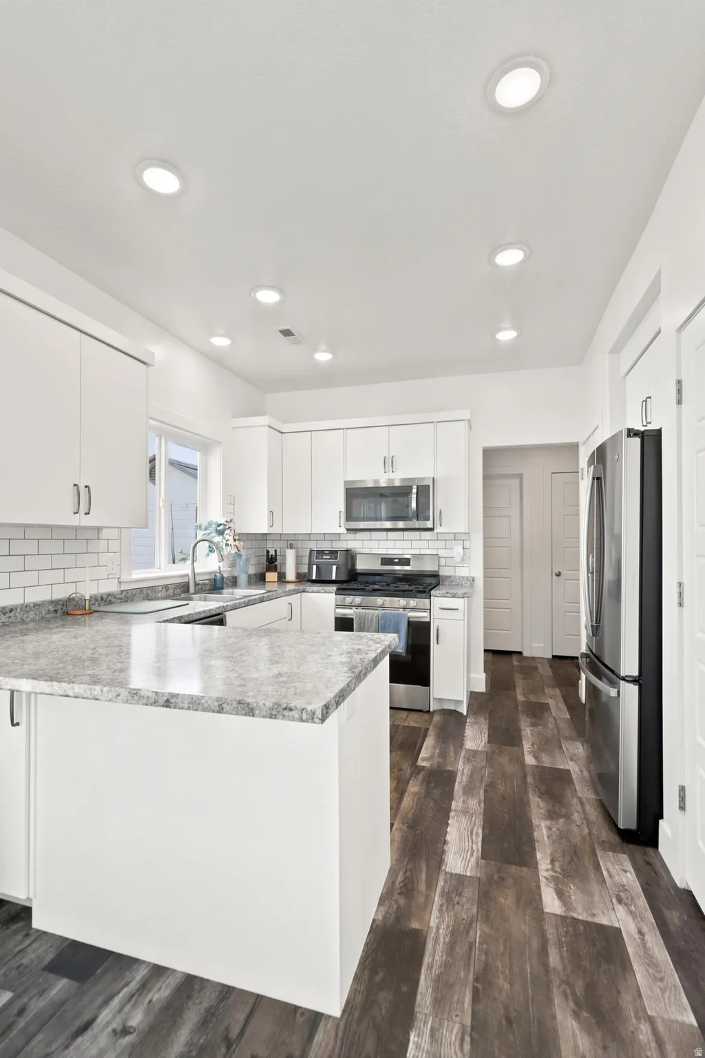 Kitchen featuring white shaker-style cabinetry, a white subway tile backsplash, stainless steel appliances, wood-finish flooring, and recessed lighting