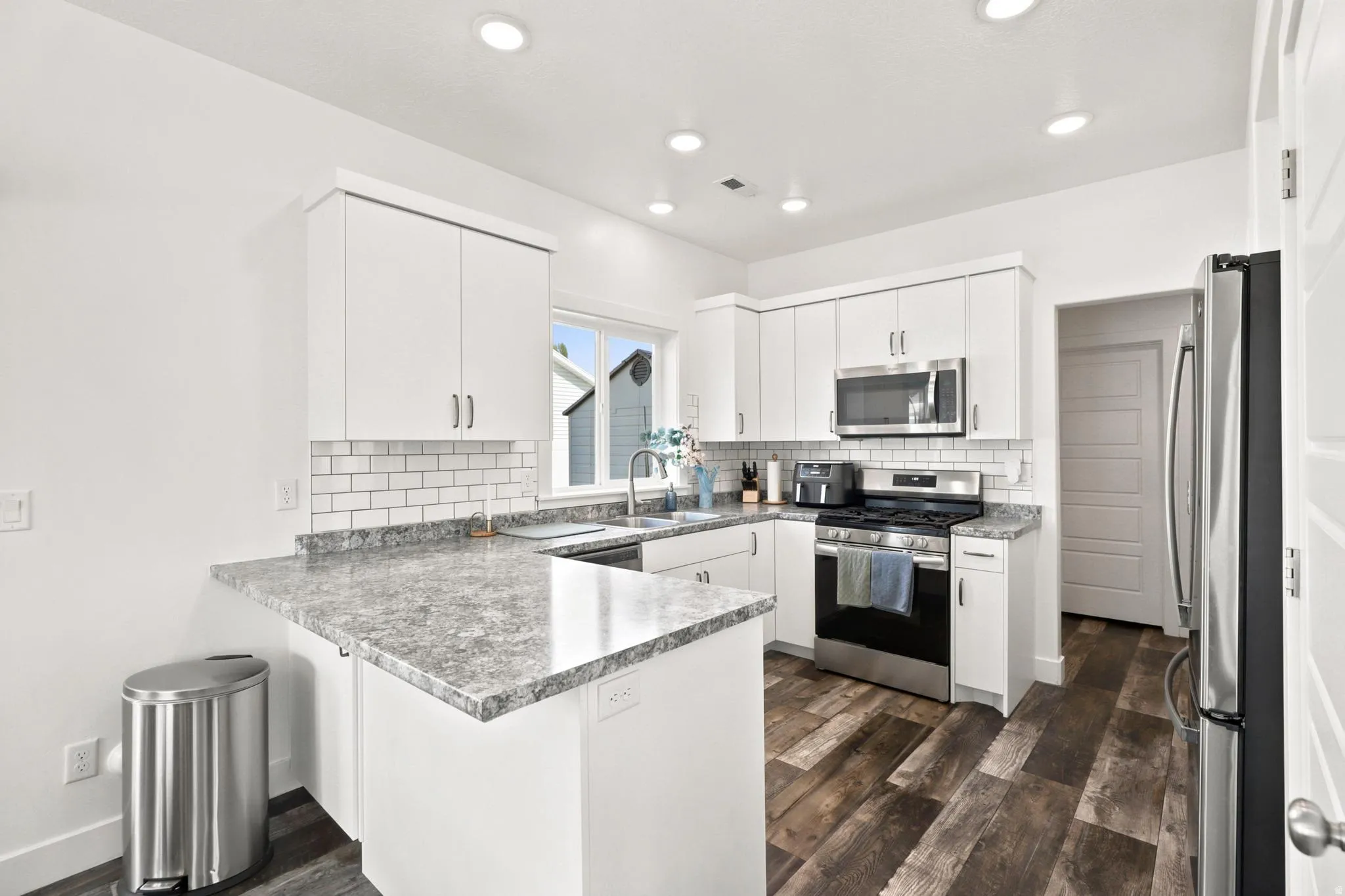 White cabinetry with stainless steel hardware, subway tile backsplash, and wood-finish flooring