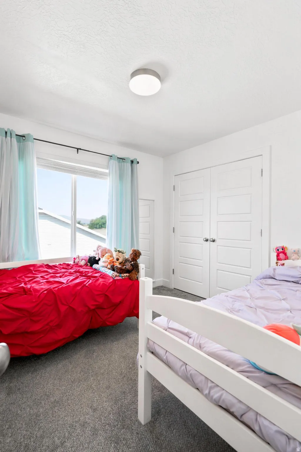 White painted walls with a textured ceiling, a flush-mount overhead light, and grey carpet flooring