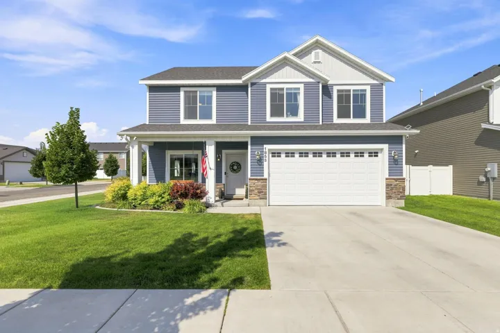 Two-story colonial home featuring a front-facing two-car garage, covered front porch with columns, and a manicured lawn with mature landscaping