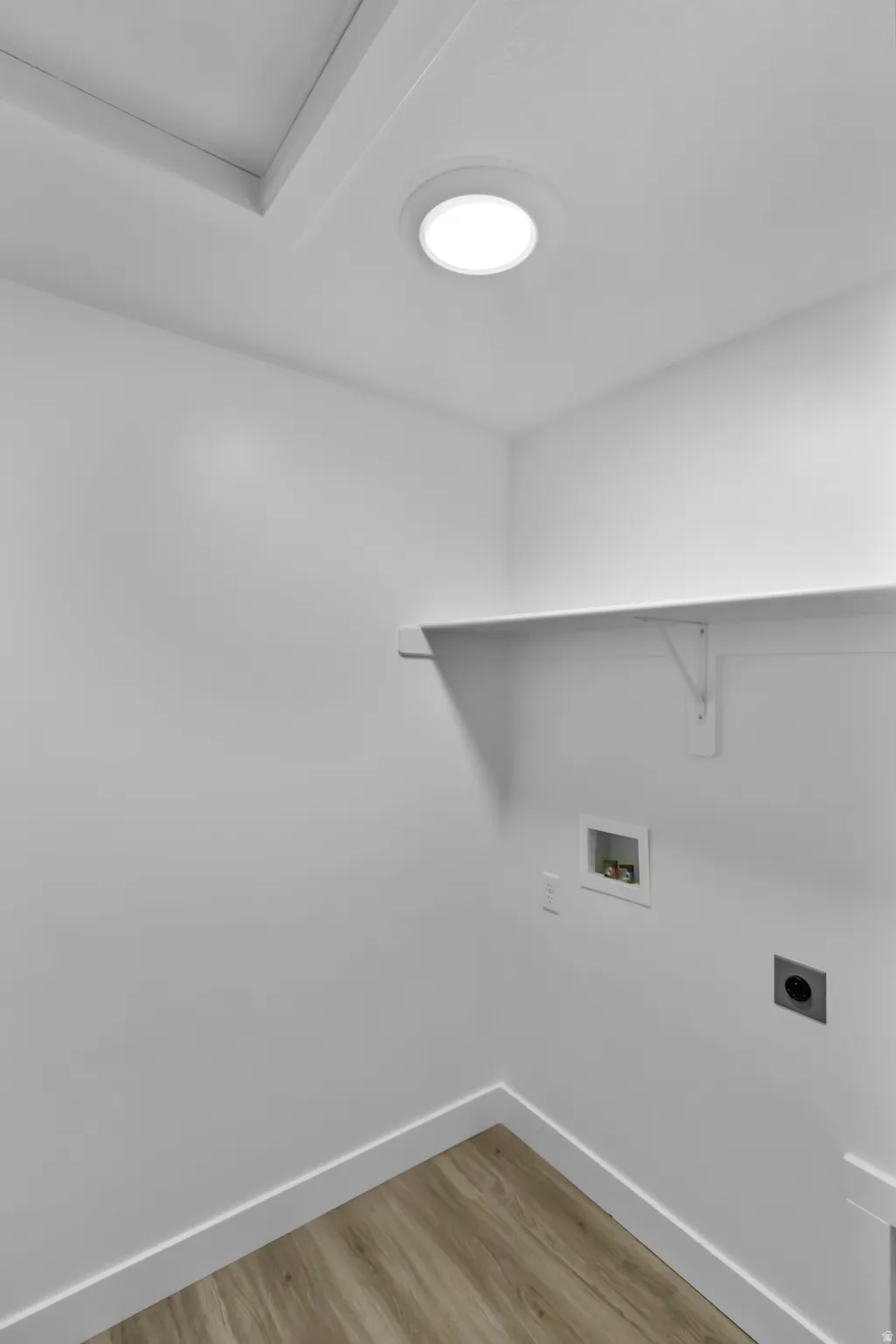 Recessed ceiling light, white walls, wood-finish flooring, built-in shelving, and laundry hookups