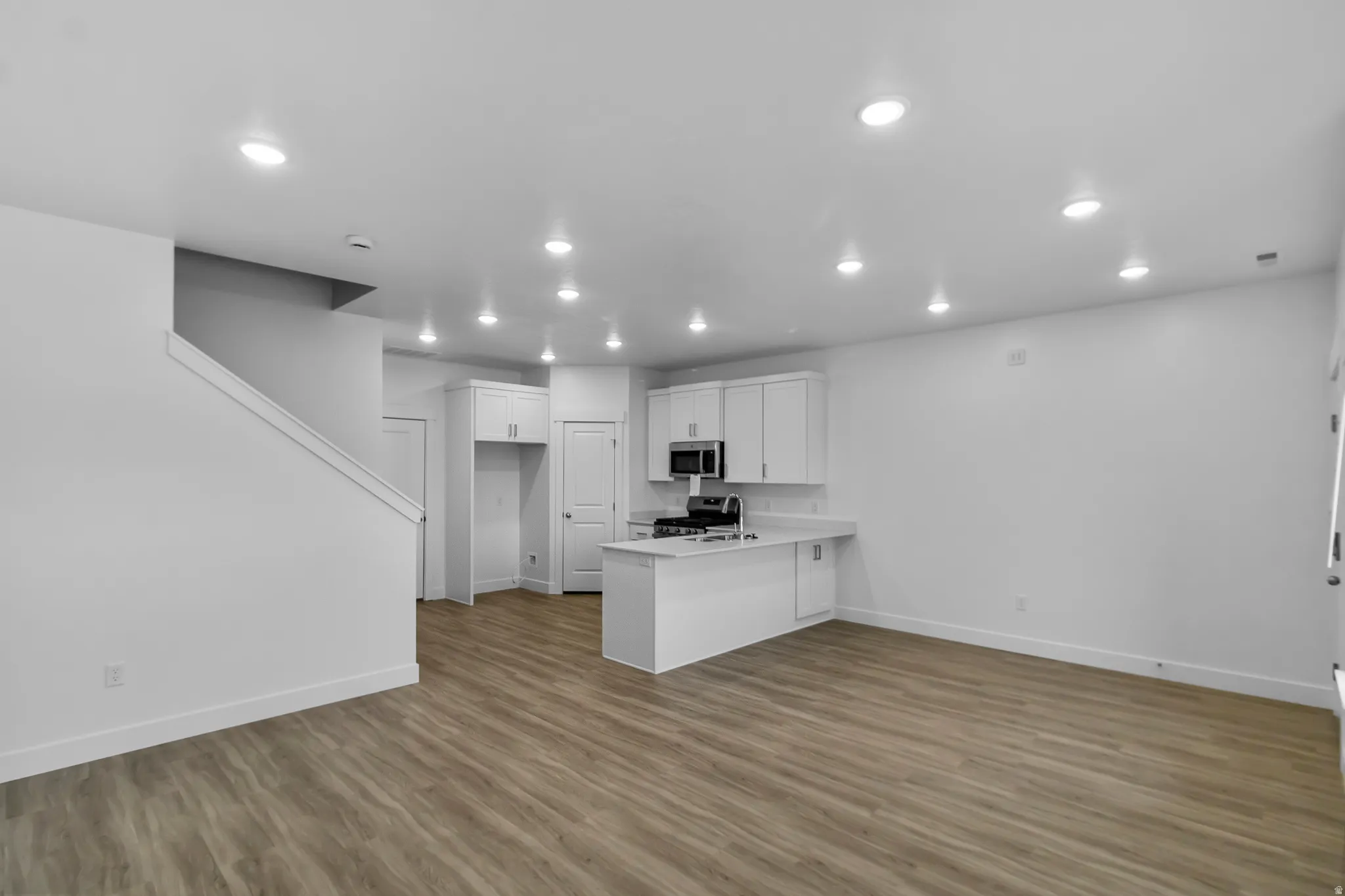 Open-concept living area with wood-finish flooring, recessed lighting, and a kitchen featuring white cabinetry, stainless steel appliances, and a gas range