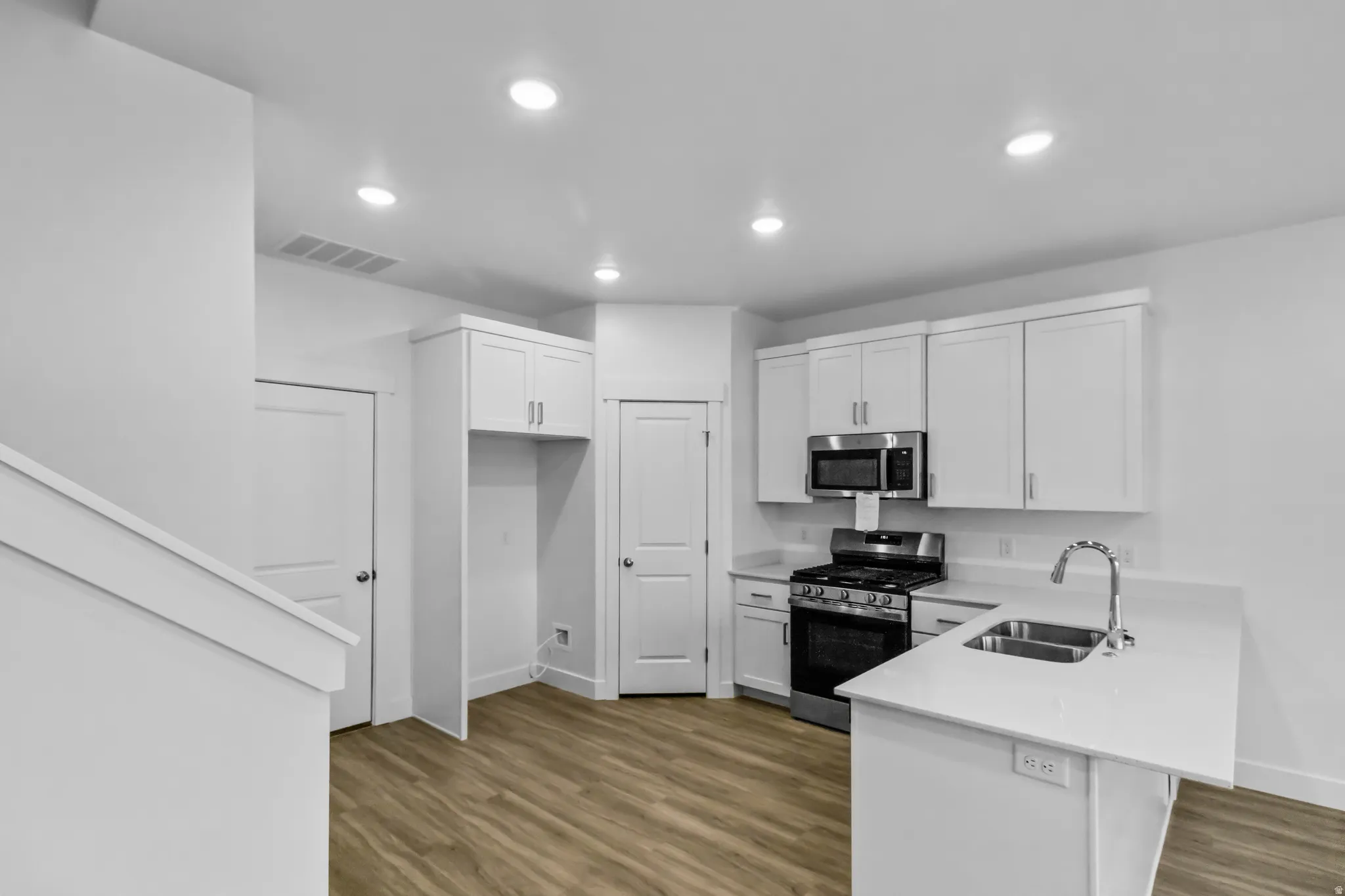 Contemporary kitchen featuring white cabinetry, stainless steel appliances, light-toned countertops, wood-finish flooring, and recessed lighting