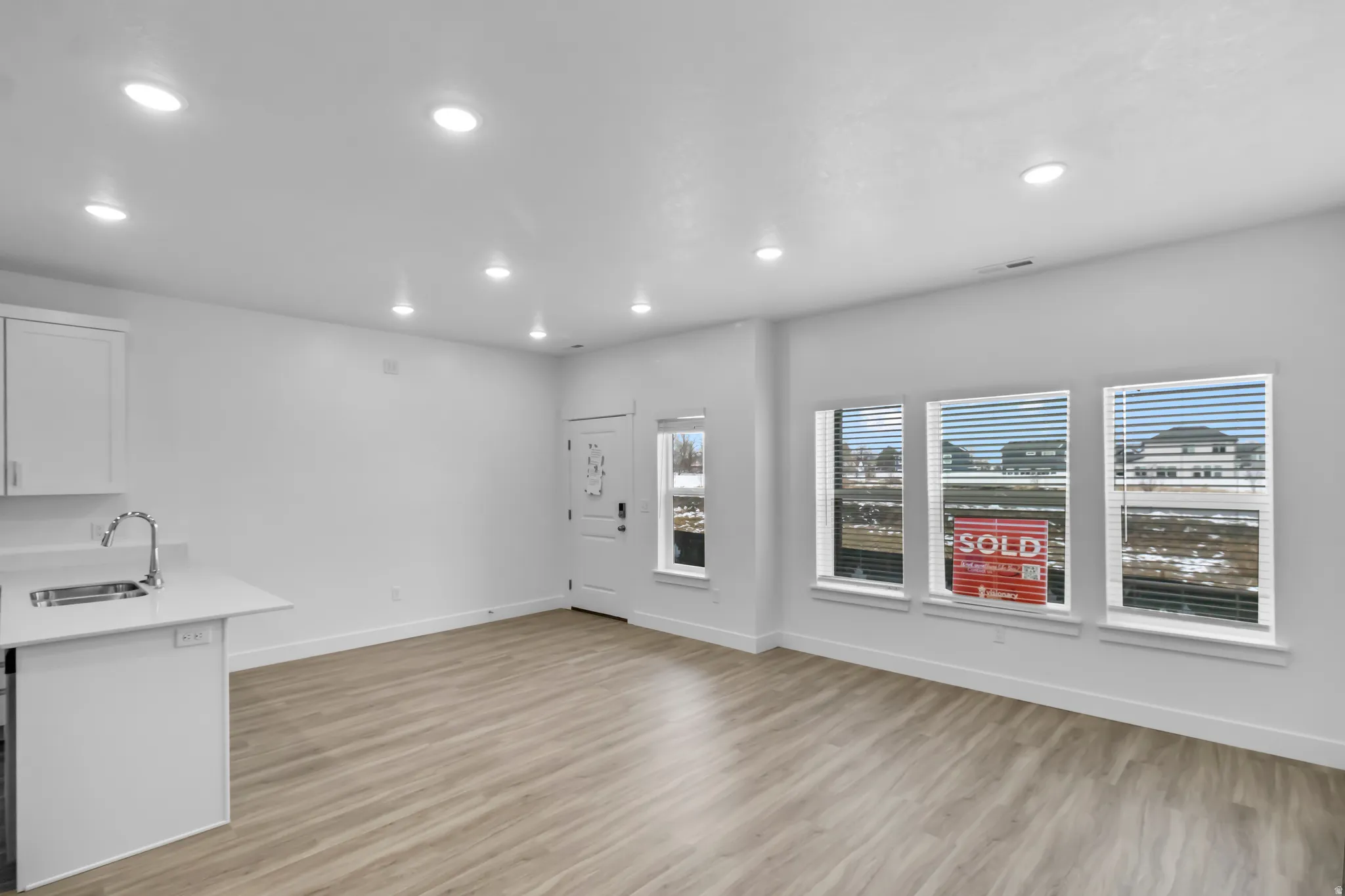 Wood-finish flooring, recessed lighting, white cabinetry, integrated sink, and multiple windows with blinds