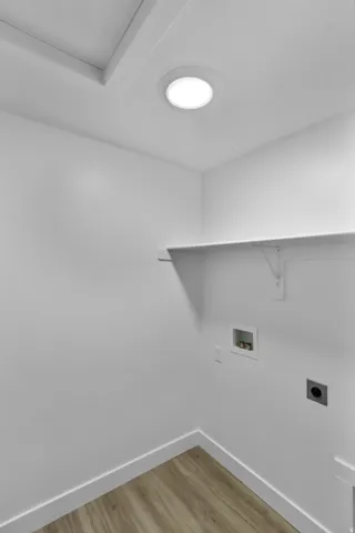 Recessed ceiling light, white walls, wood-finish flooring, built-in shelving, and laundry hookups
