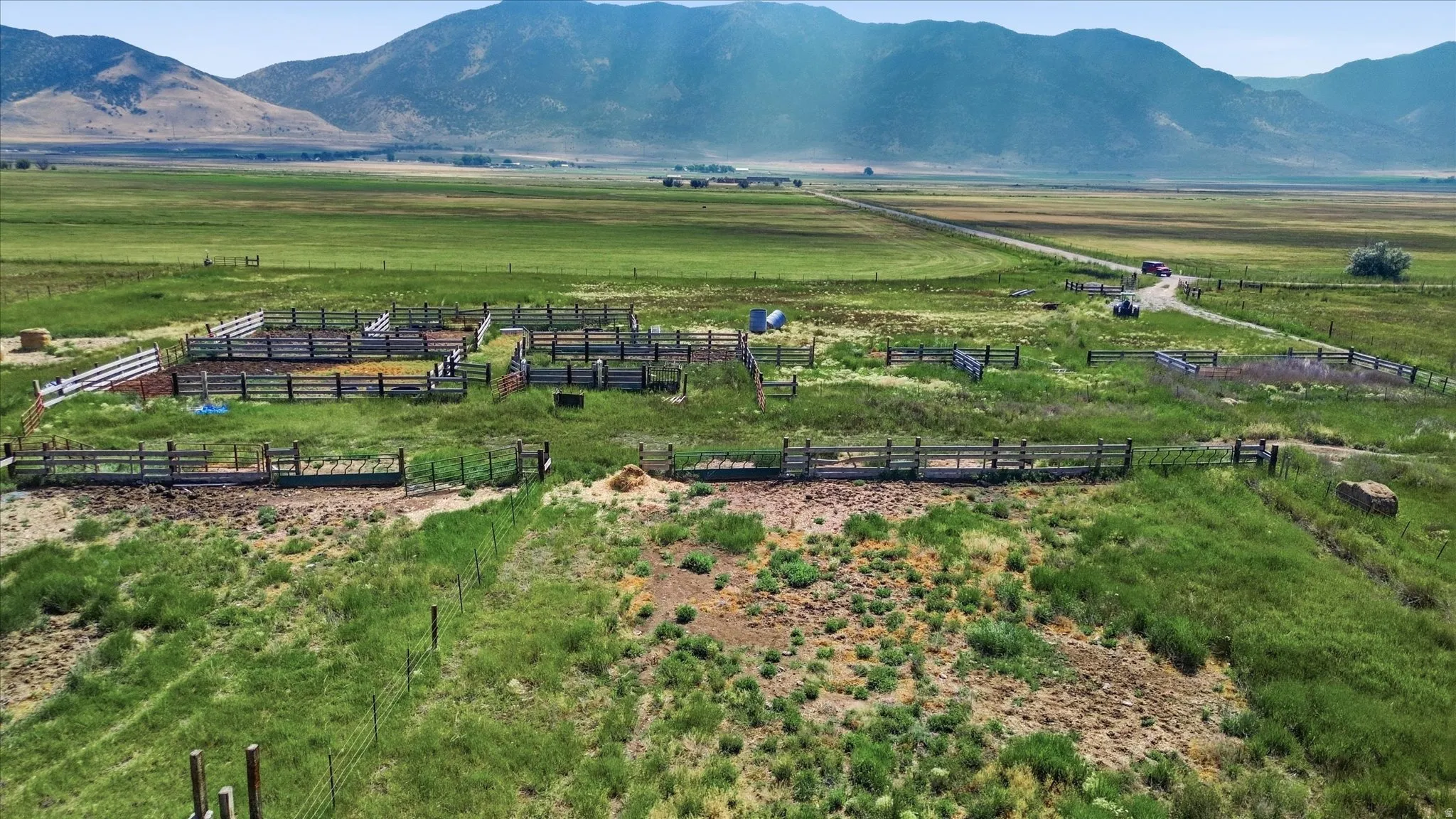 Expansive open land with a dirt road, multiple fenced enclosures, and distant mountainous terrain