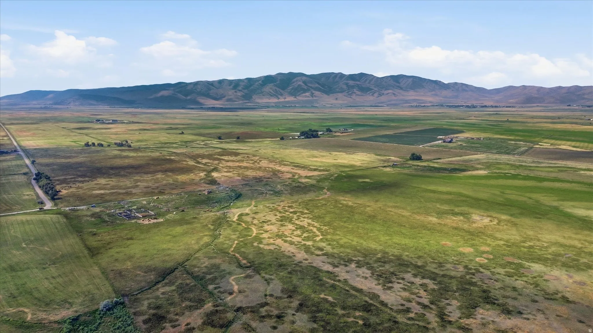 Expansive rural landscape featuring a distant mountain range, agricultural fields, and scattered farm structures