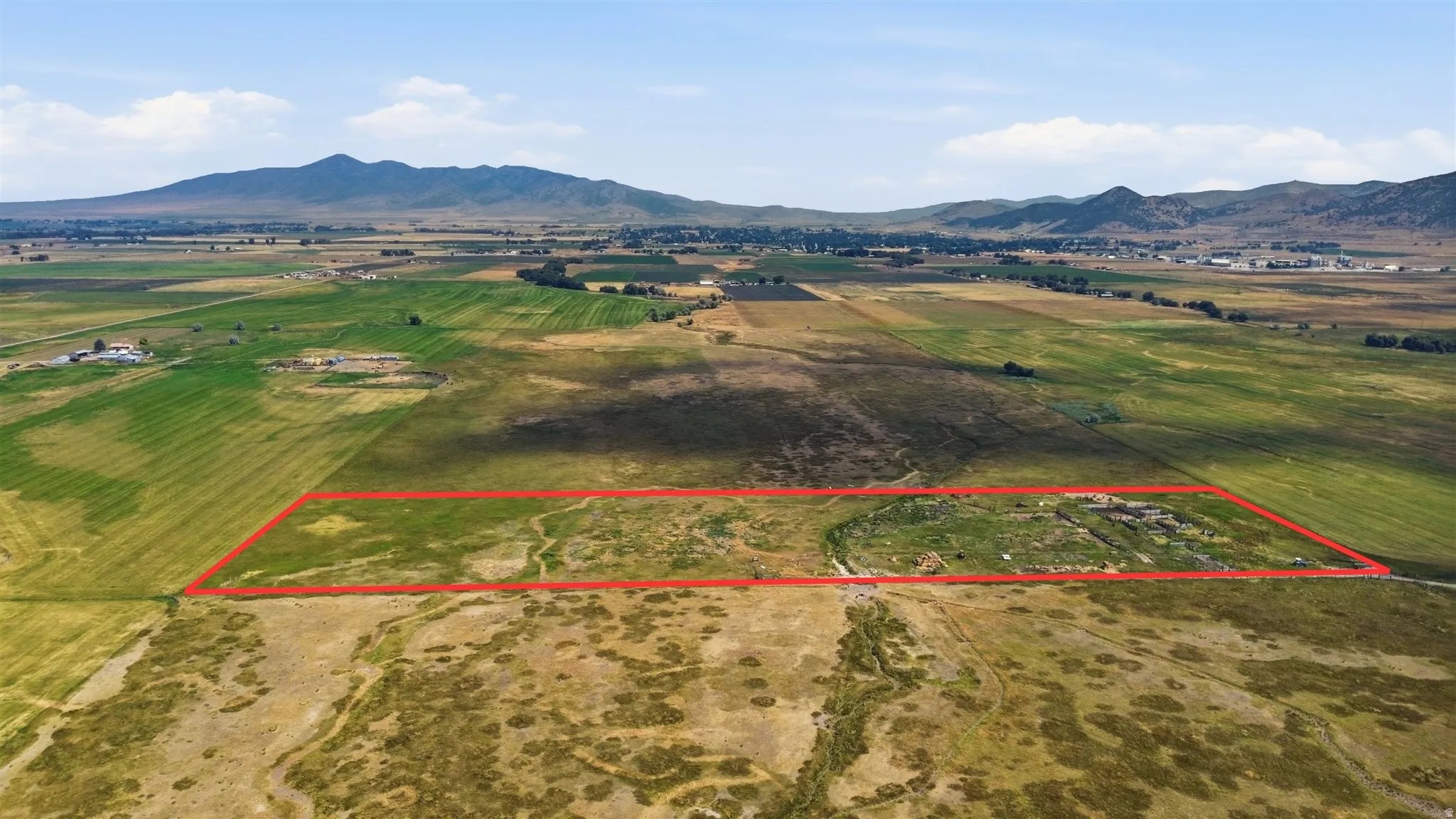 Expansive agricultural land featuring a natural water channel and distant mountain scenery