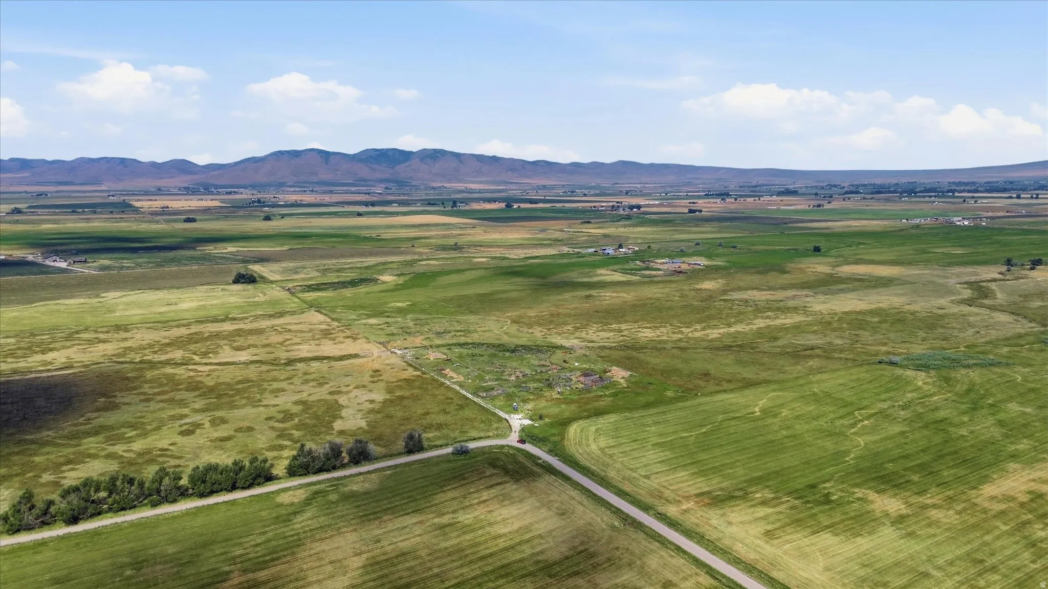 Expansive green fields with a visible road and distant mountains
