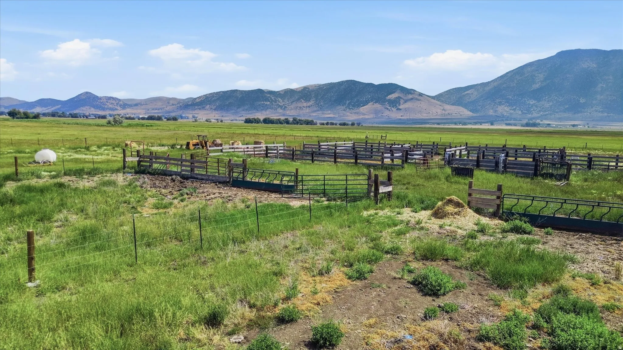 Expansive agricultural property featuring fenced enclosures, lush green pasture, and distant mountain scenery