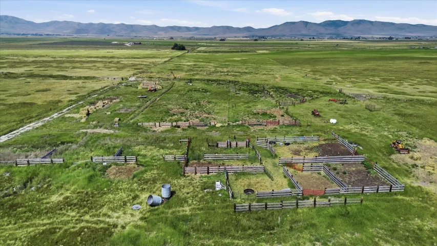 Expansive green acreage featuring multiple fenced enclosures, distant agricultural fields, and a mountain range backdrop