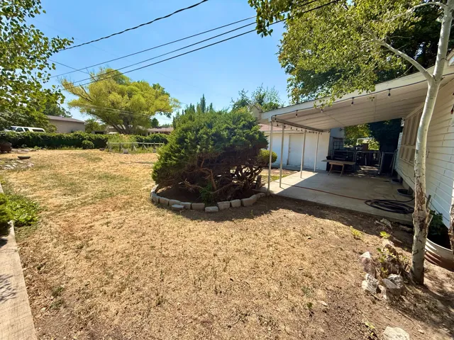 Expansive outdoor space featuring a covered patio, mature trees, and a concrete paver garden border