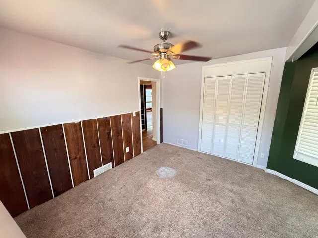 Carpeted room featuring wood paneling, a ceiling fan with light, and bi-fold closet doors