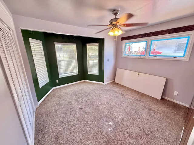 Recessed bay window, ceiling fan with integrated lighting, wood-finish window valance, and carpeted flooring