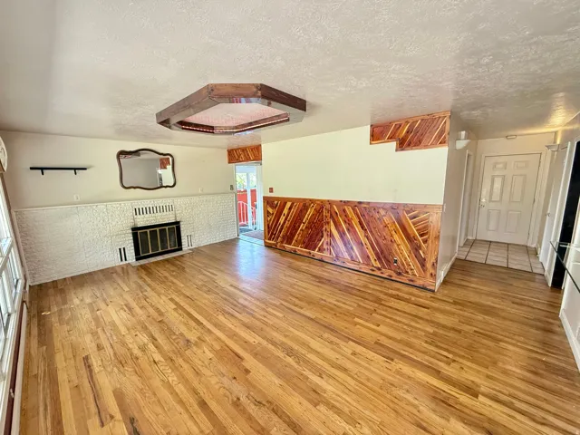 Hardwood-finish flooring, white painted brick fireplace with black metal insert, decorative wood paneling, wood-finish ceiling light fixture, and a paneled entry door