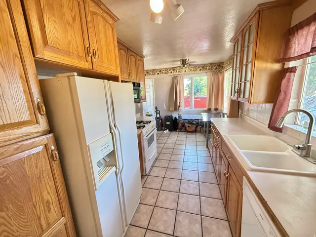 Kitchen featuring wood cabinetry, a double basin sink, tile flooring, and white appliances