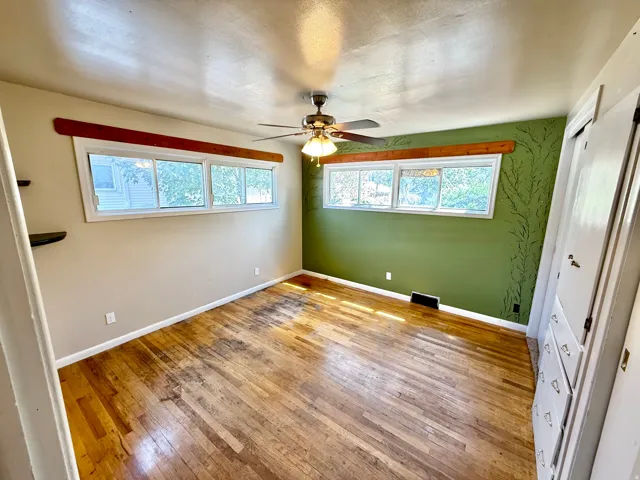 Hardwood flooring, multiple windows providing illumination, ceiling fan with integrated lighting, built-in cabinetry, and wall-mounted shelving