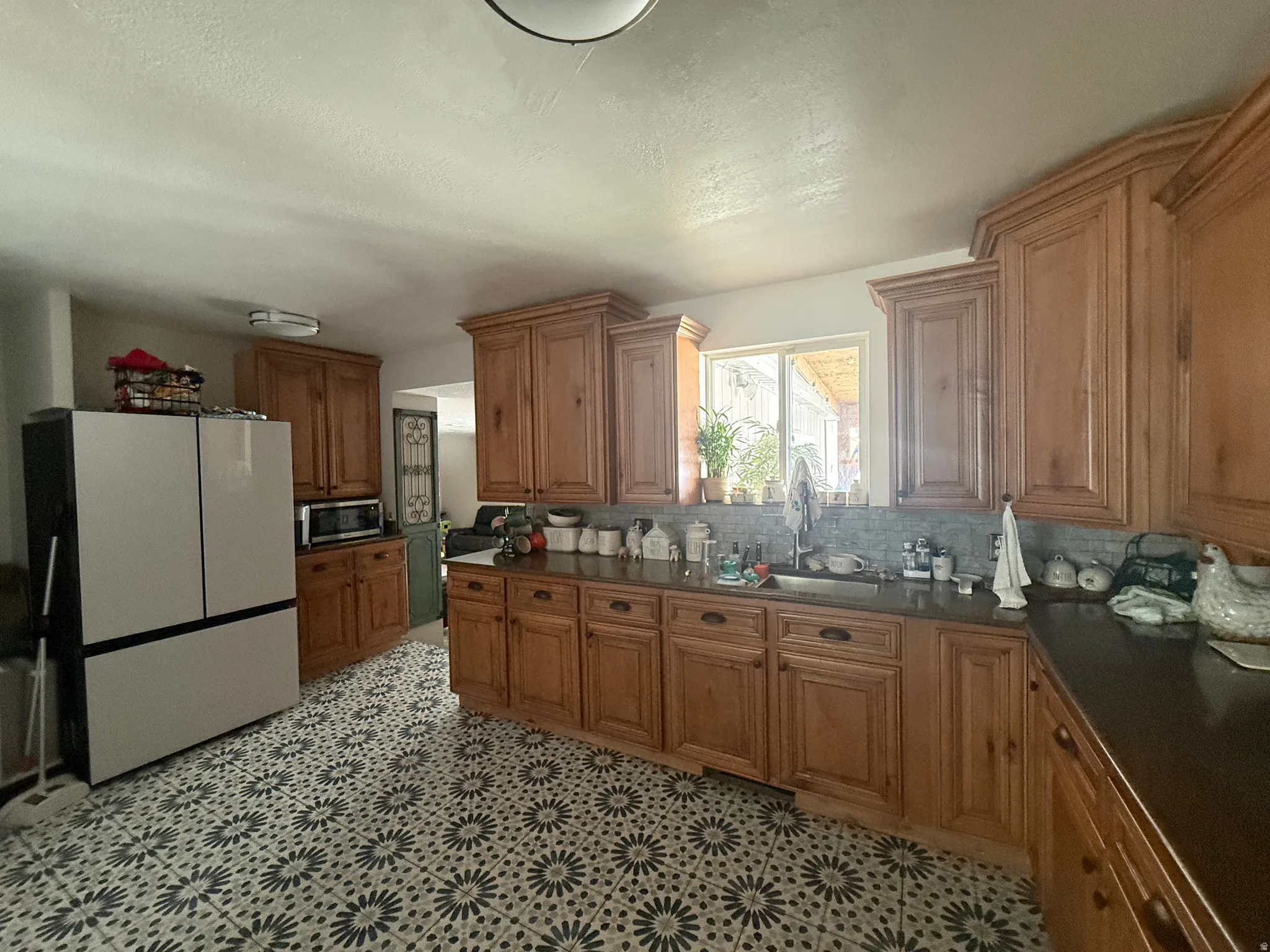 Kitchen featuring wood-finish cabinetry, solid surface countertops, patterned flooring, and a tiled backsplash