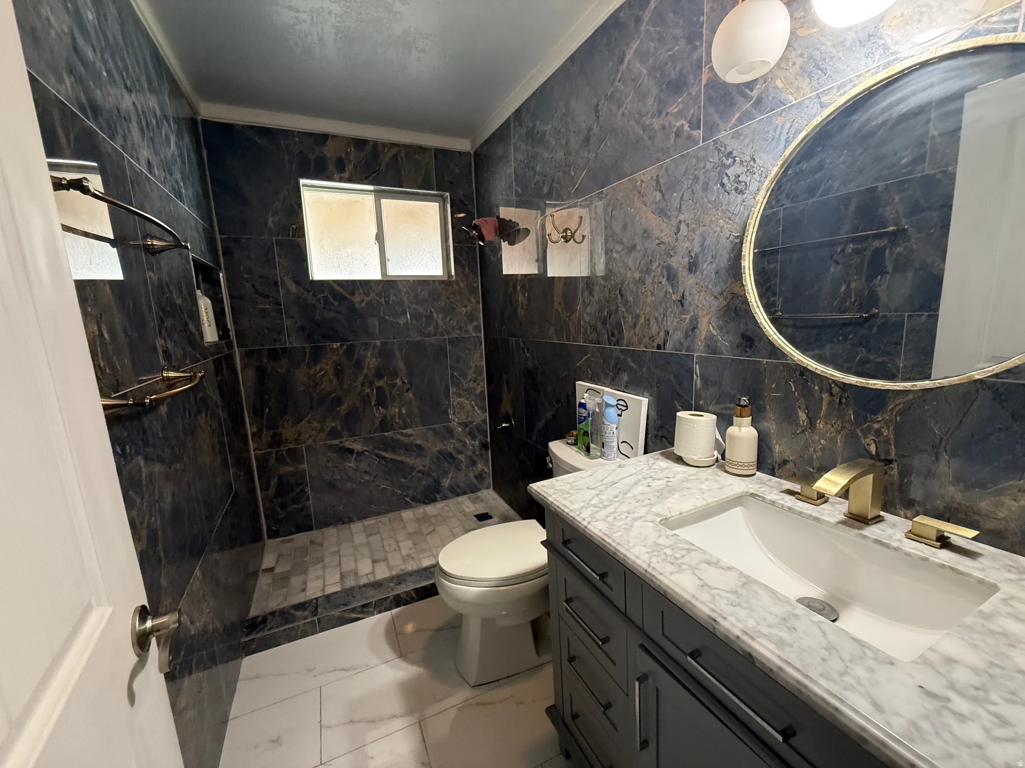 Walk-in shower with dark marbled wall tile and mosaic floor tiling