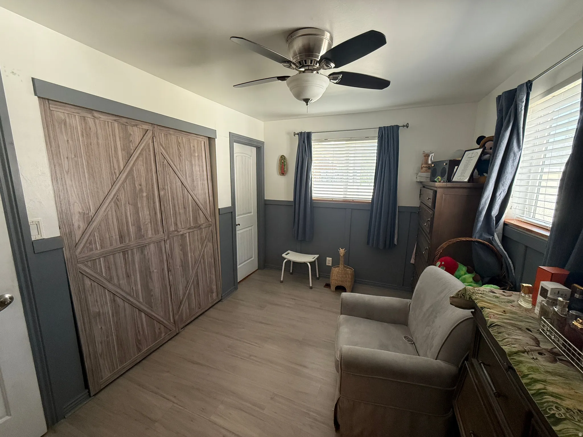 Wood-finish flooring, ceiling fan with integrated lighting, wood-finish bi-fold closet doors, and wainscoting with board and batten detailing