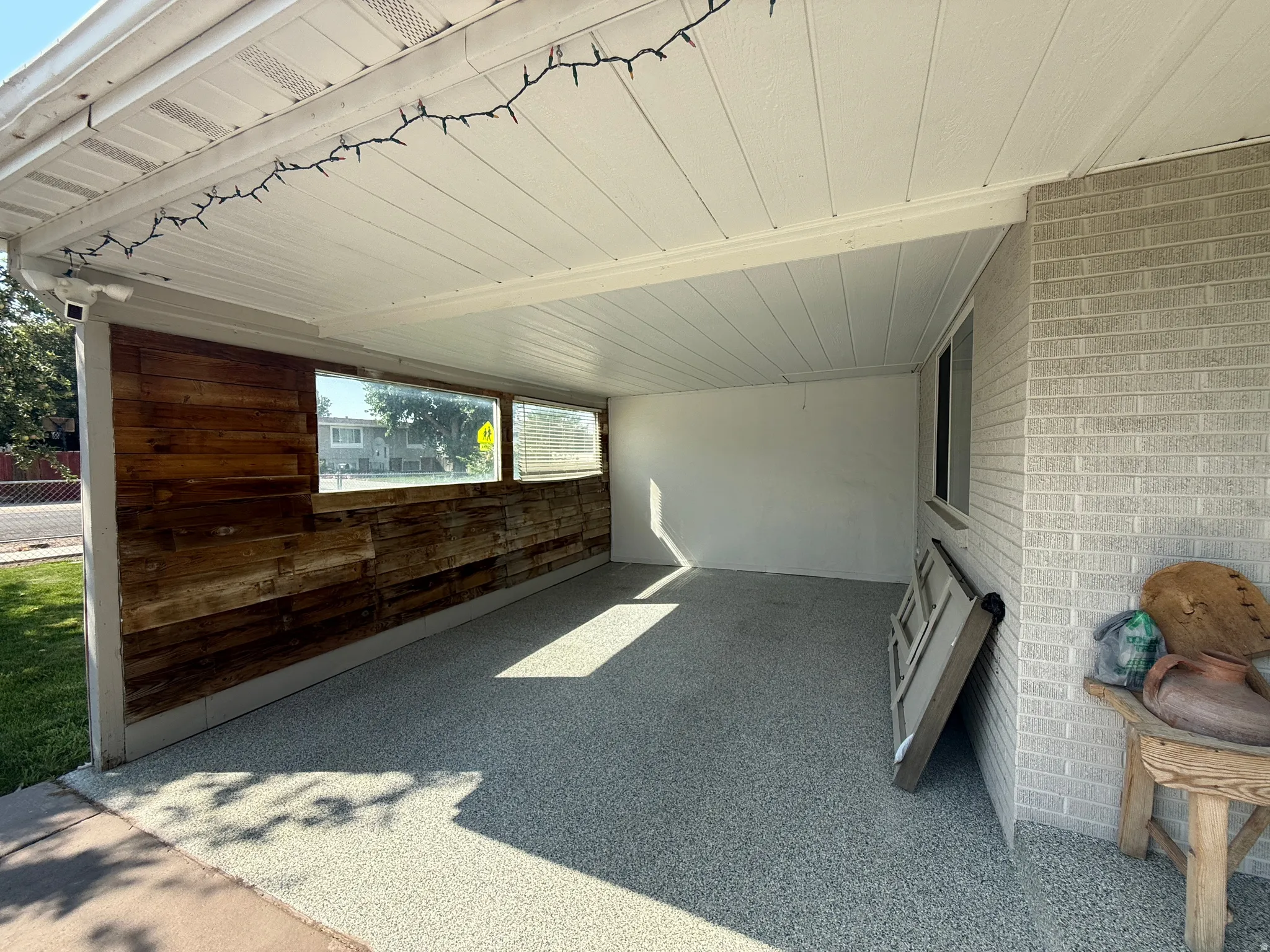 Attached covered patio featuring a textured floor finish, wood-plank accent wall, and horizontal window panels