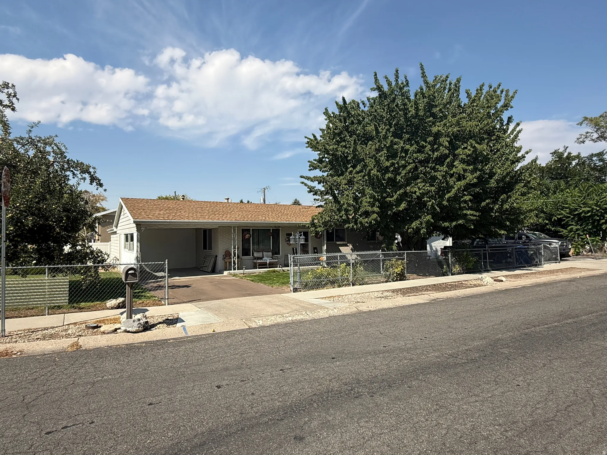 Single-story residence featuring a carport, chain-link fencing, and mature landscaping