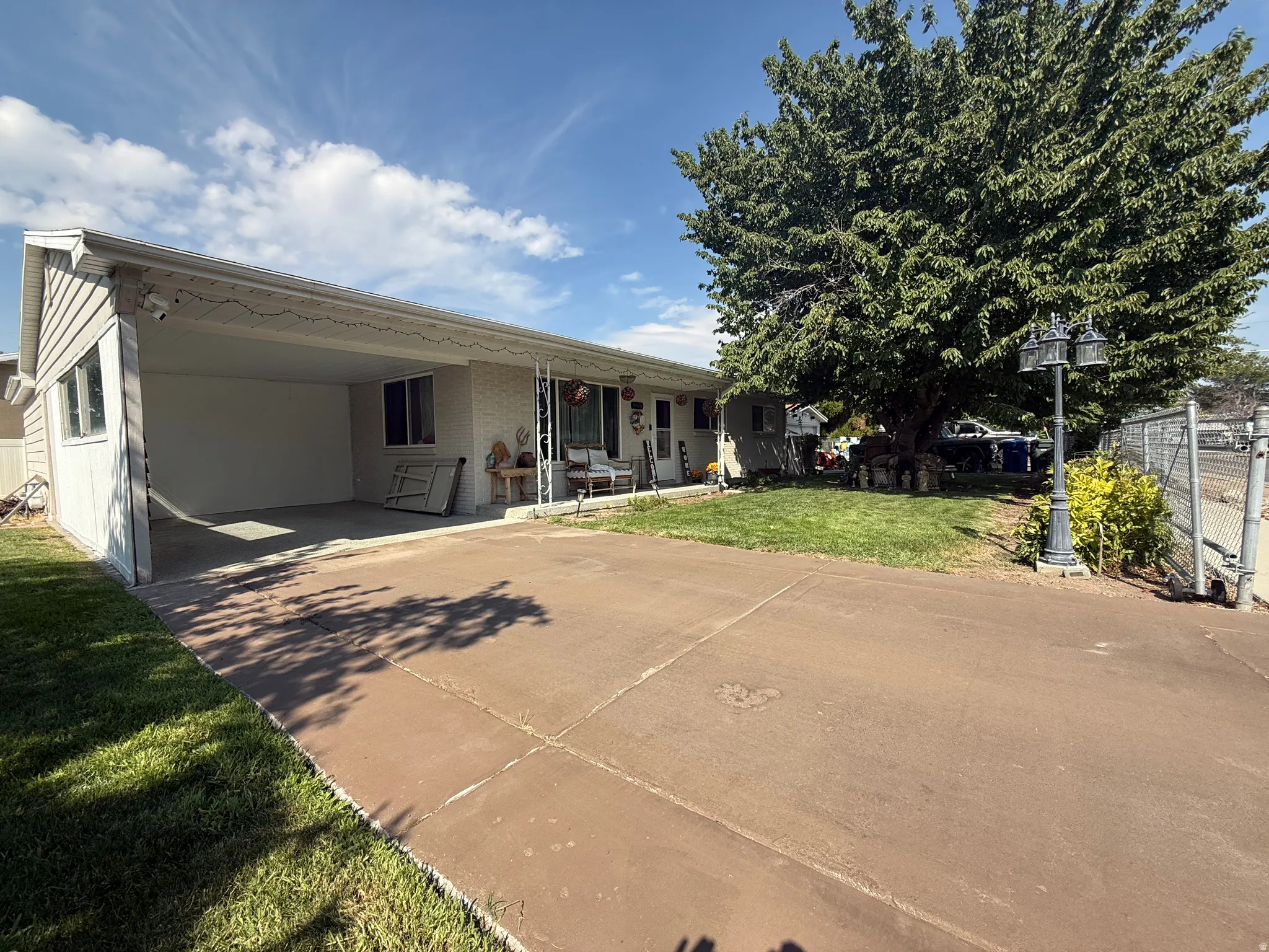 Covered carport with concrete flooring, mature landscaping, fenced perimeter, and a concrete driveway