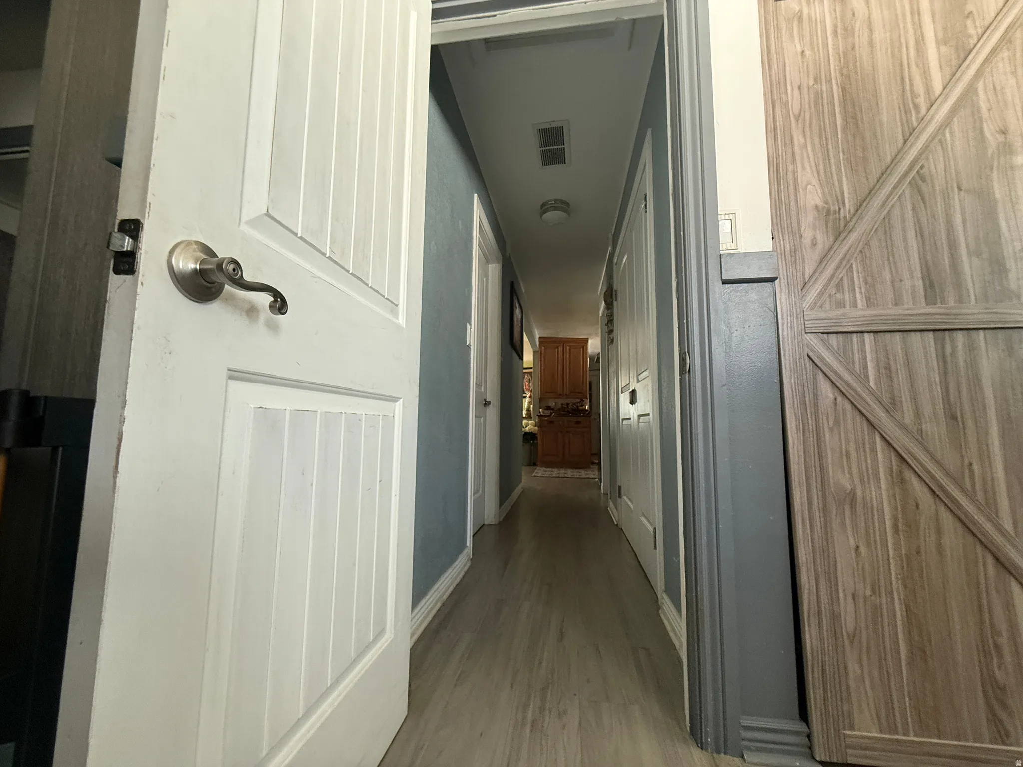 Hallway featuring wood-finish flooring, paneled doors with brushed nickel hardware, and a barn-style door