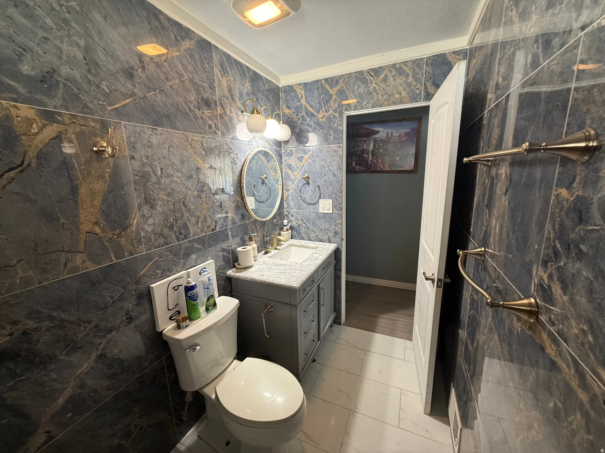 Bathroom featuring floor-to-ceiling marbled wall tiles, a single vanity with a stone countertop, a wall-mounted mirror, and white floor tiles