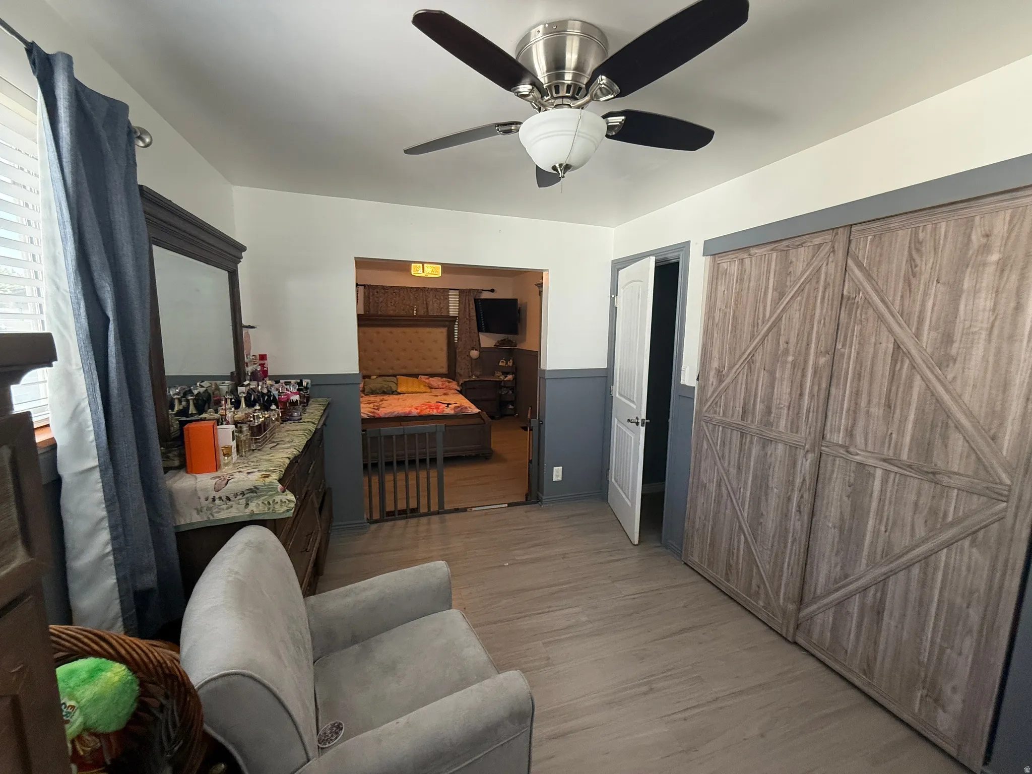 Wood-finish flooring with a ceiling fan light fixture, white interior door, and barn door style closet