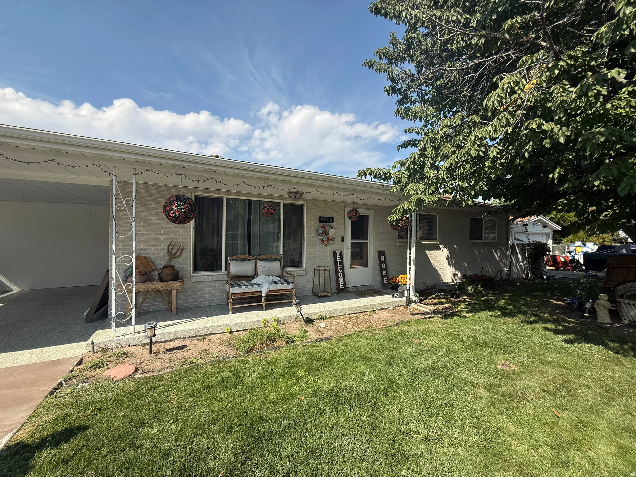 Brick exterior with a covered entry, established front yard, mature tree, and a covered carport with concrete flooring