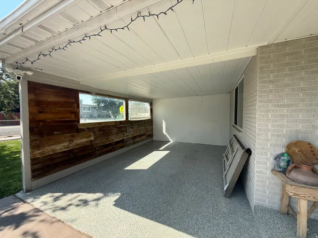 Attached covered patio featuring a textured floor finish, wood-plank accent wall, and horizontal window panels
