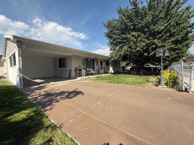 Covered carport with concrete flooring, mature landscaping, fenced perimeter, and a concrete driveway