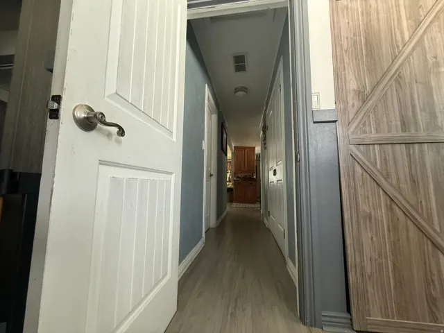 Hallway featuring wood-finish flooring, paneled doors with brushed nickel hardware, and a barn-style door
