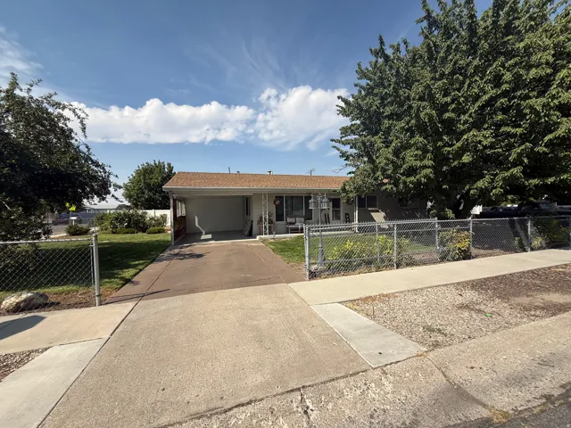 Single-story residence with a covered carport, chain-link fencing, and mature trees