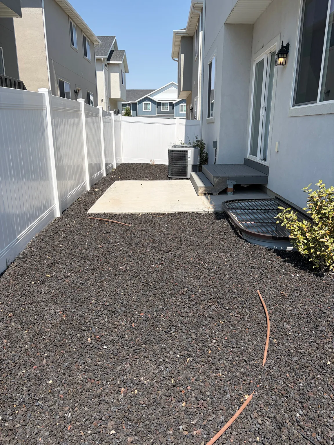 Private outdoor space featuring a white vinyl fence, dark aggregate ground cover, and a concrete patio pad