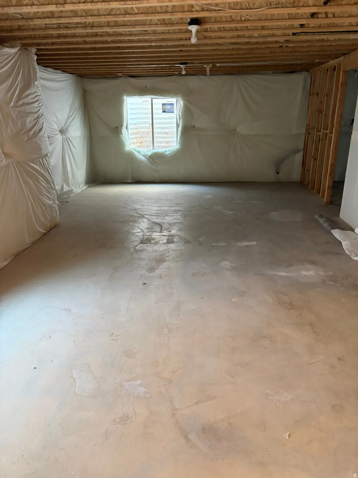 Unfinished basement with exposed ceiling joists, concrete flooring, and an egress window