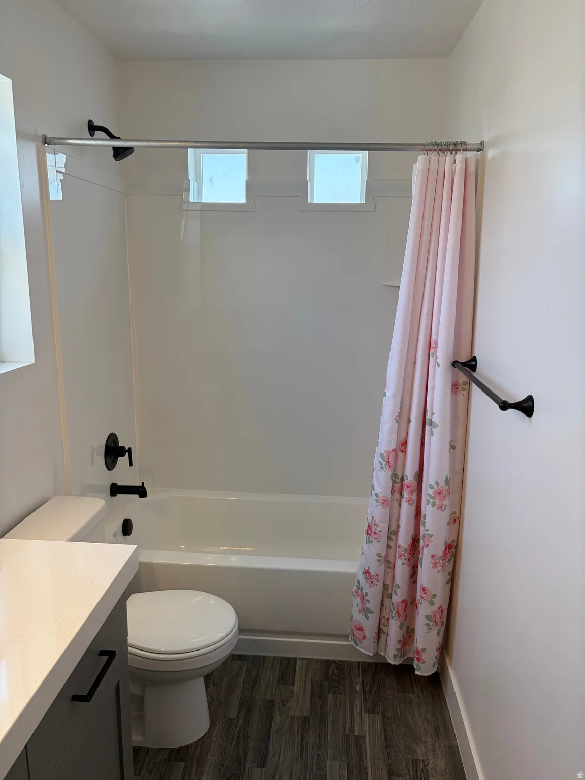 Bathtub with dark-toned fixtures, wood-finish flooring, and a vanity with a light-toned countertop