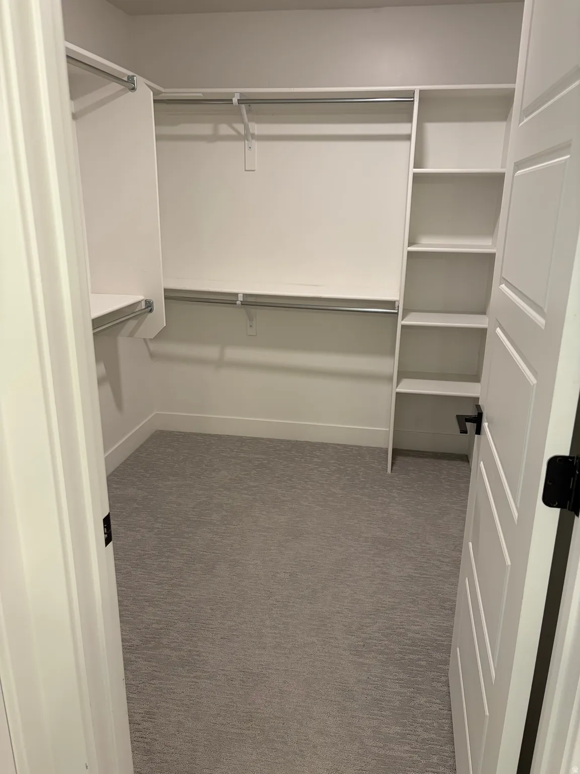 Walk-in closet featuring built-in shelving, multiple hanging rods, and grey patterned carpeting