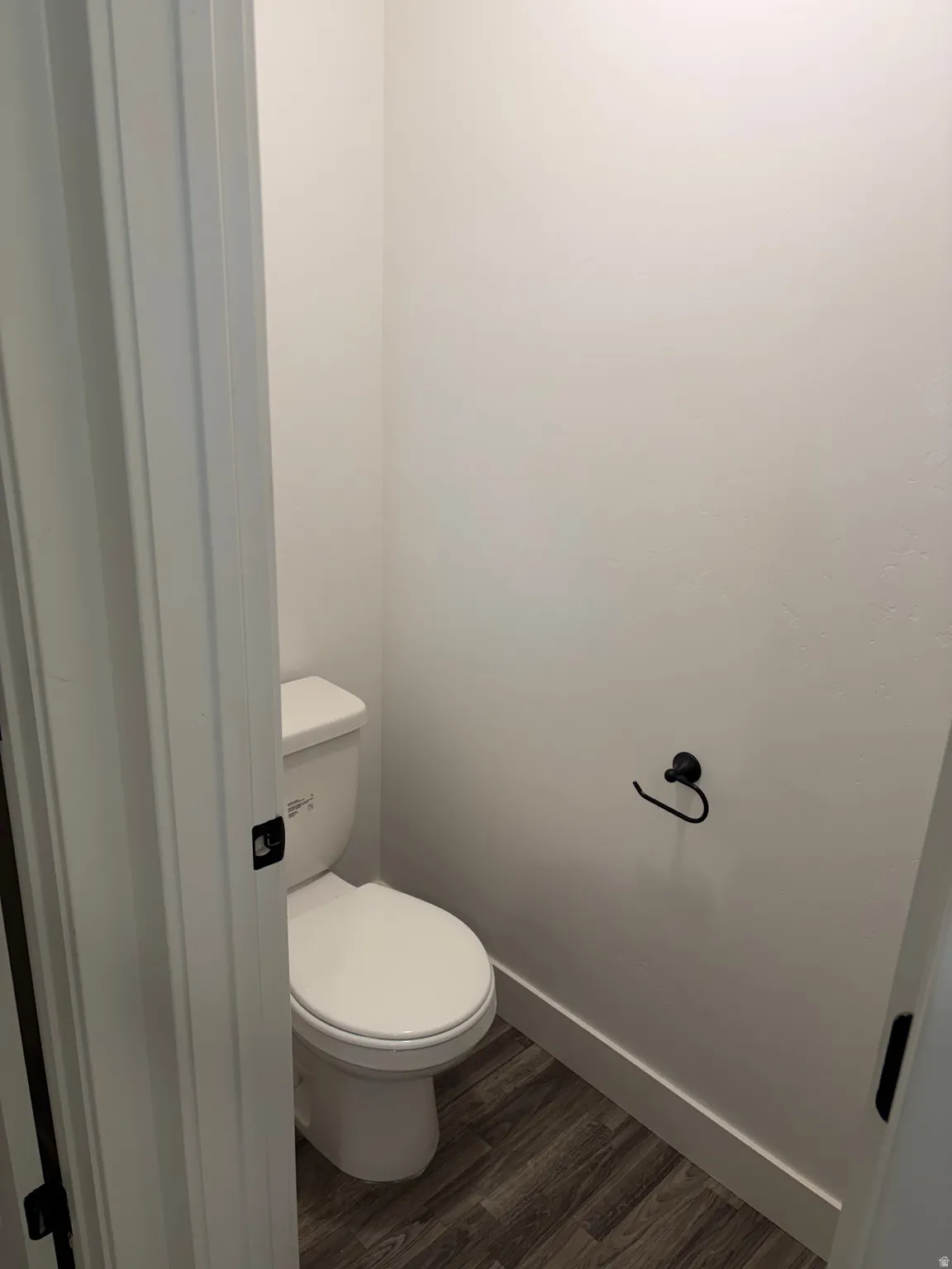 White walls with matching trim, dark wood-finish flooring, and a white toilet with matte black hardware