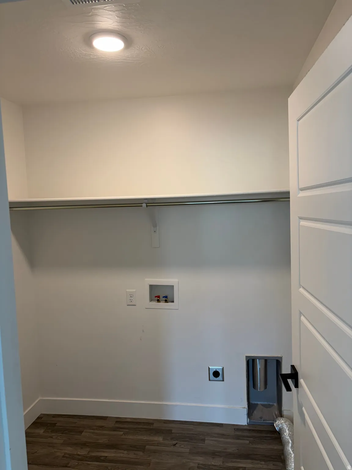 Dedicated laundry space with wood-finish flooring, overhead shelving, and a modern flush-mount ceiling light