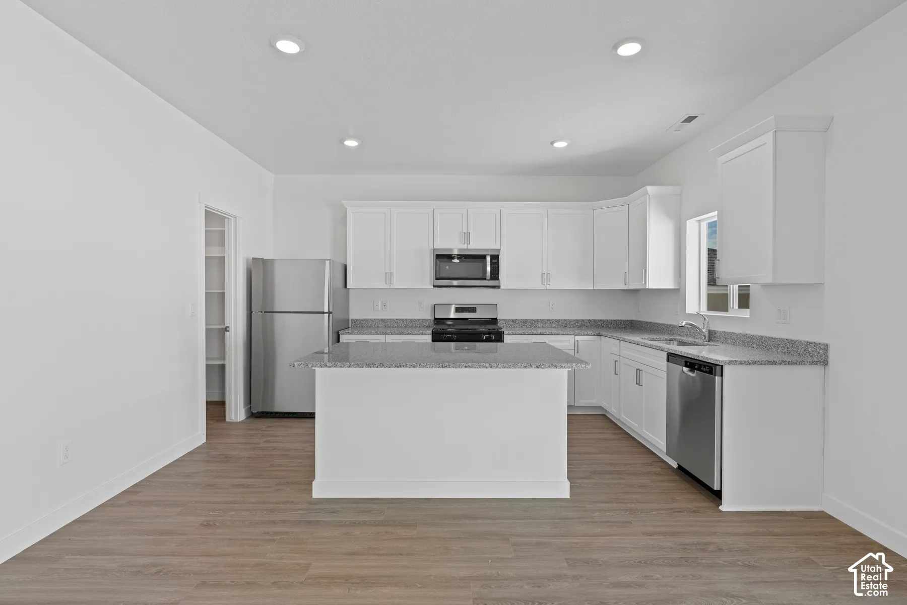 Kitchen featuring white cabinetry, stainless steel appliances, a center island, and wood-finish flooring